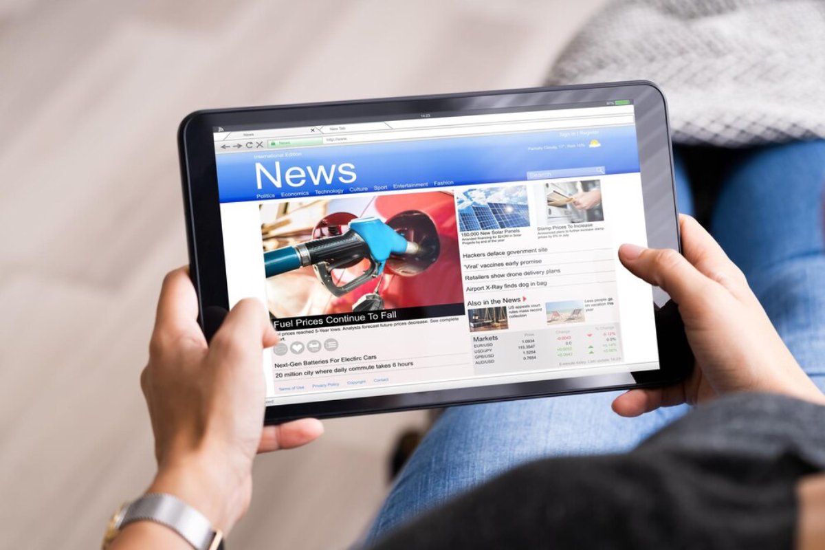A person holding a tablet displaying a news website with articles on fuel prices, electric cars, and current events.