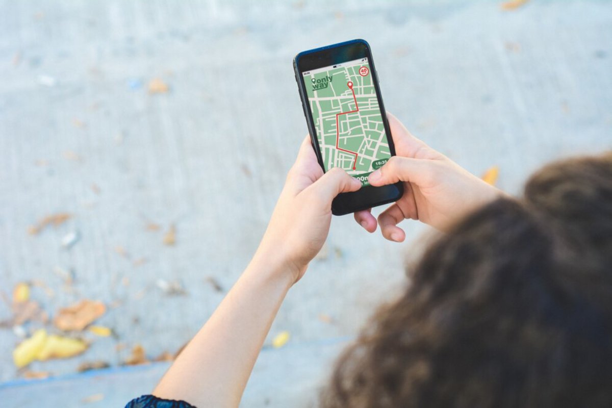A person holding a smartphone displaying a detailed map with a highlighted route, while outdoors on a textured surface.