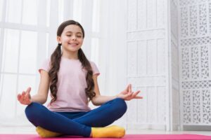 A girl sits in a yoga pose, demonstrating focus and tranquility in a serene environment.