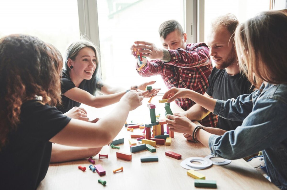 A group of people collaboratively building a colorful tower with stacking blocks on a wooden table, focused and engaged in the activity.