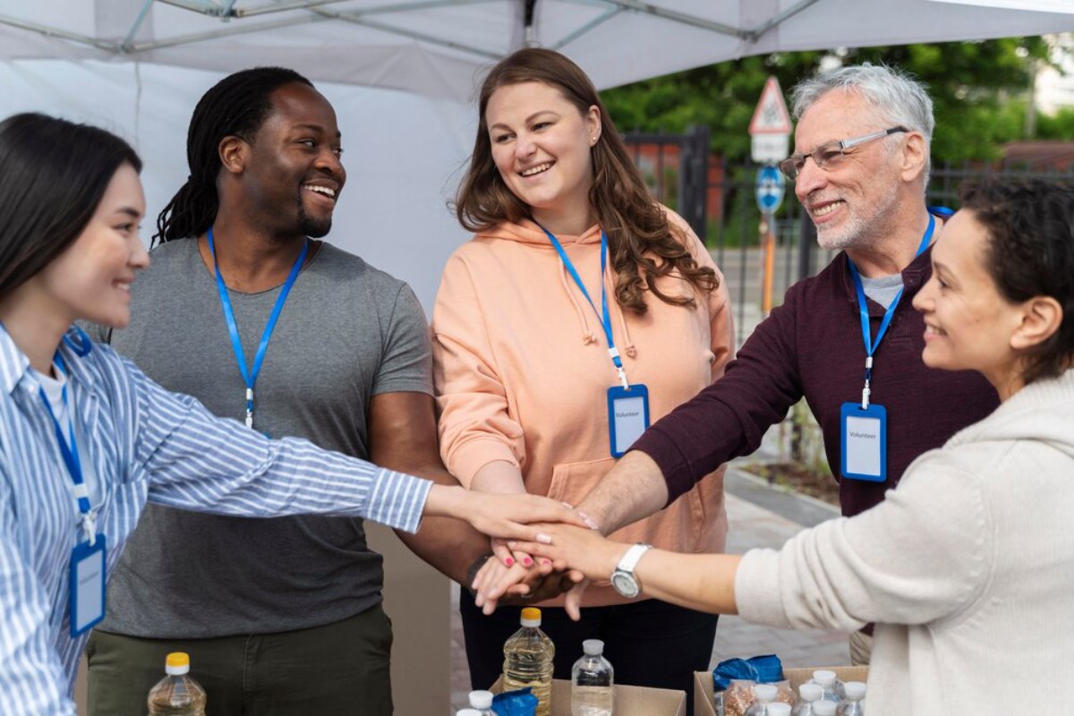 A group of volunteers with blue name tags join hands over a table with bottles and snacks, showcasing teamwork and collaboration.