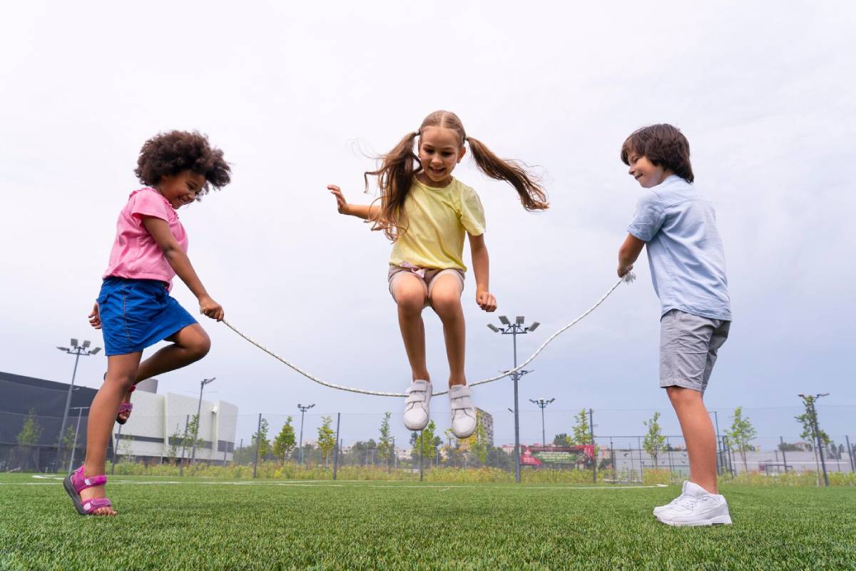 Three children joyfully playing together with a skipping rope in a sunny outdoor setting.