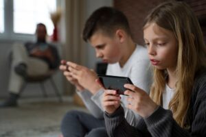 Two individuals sit closely together on the floor, each absorbed in their smartphones, with a relaxed atmosphere in the background.