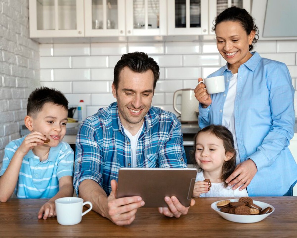 Family of four enjoying cookies and screen time in a bright kitchen.