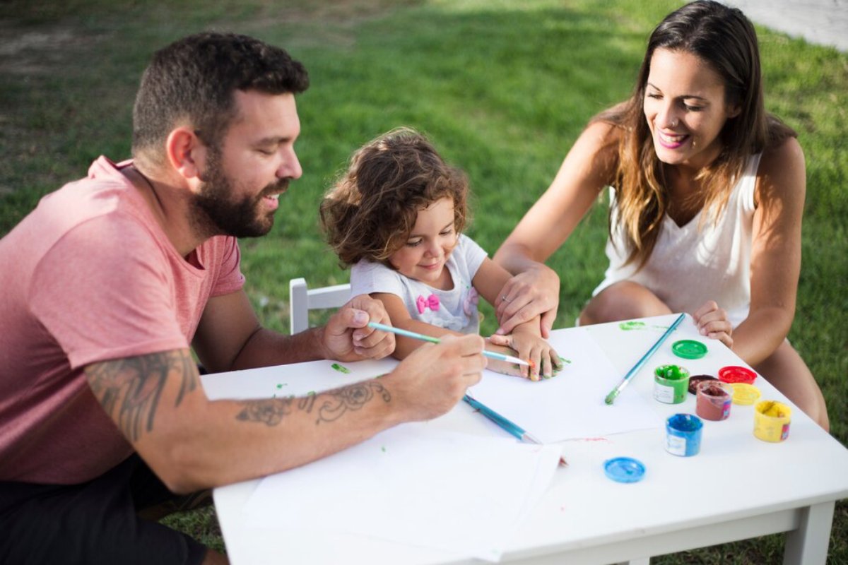 A family with a young child painting together outdoors on a sunny day.
