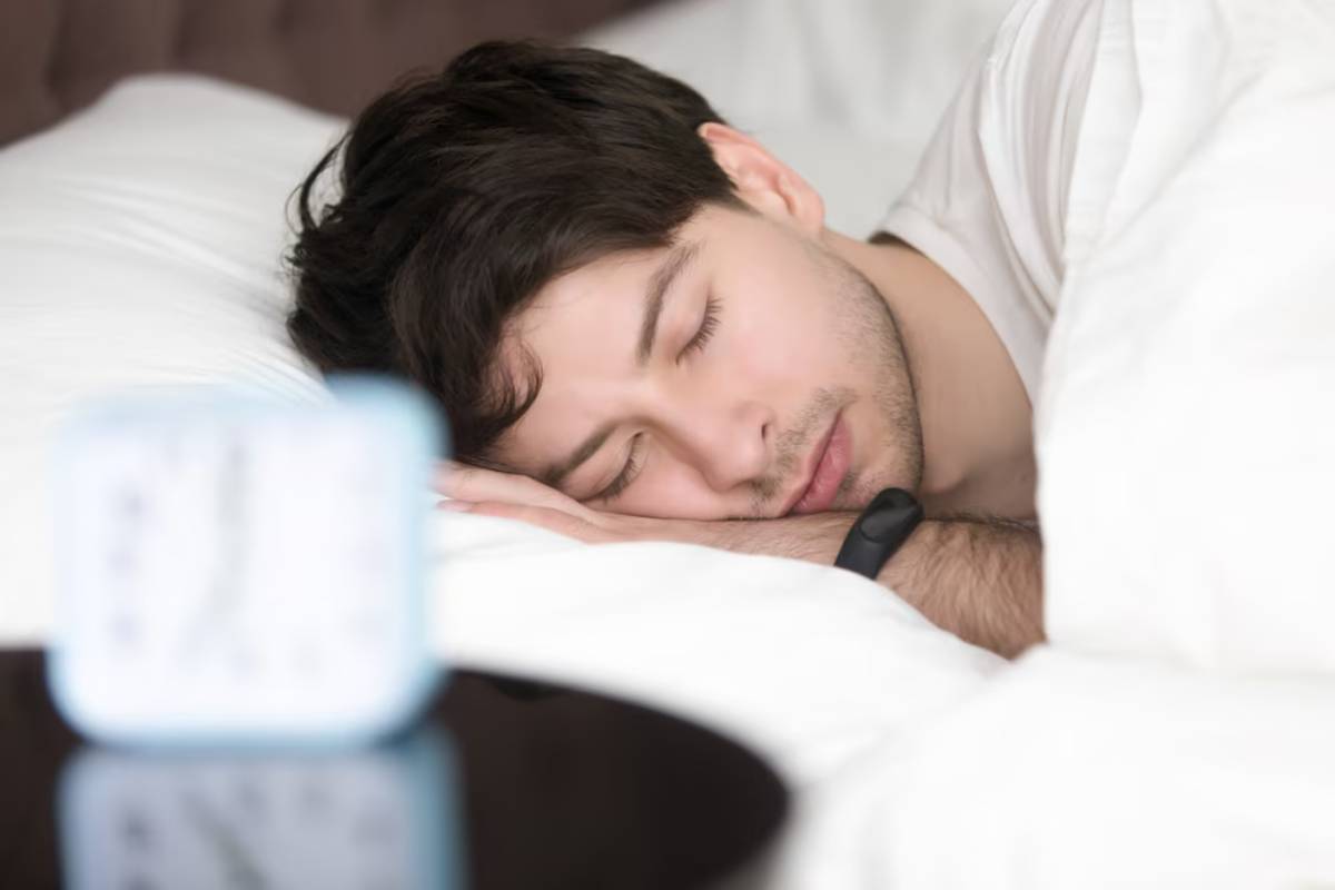 Young man peacefully sleeping in bed with a blurred alarm clock in the foreground.