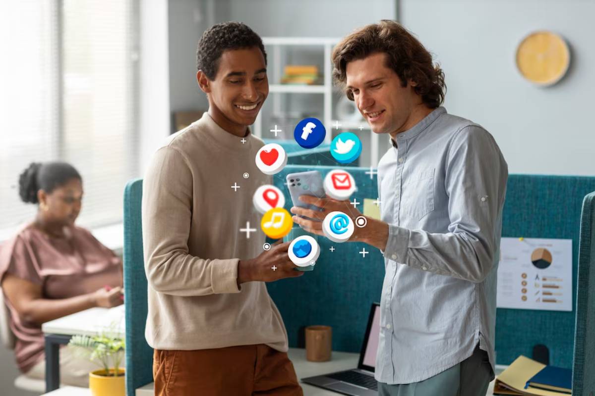 Two men happily discussing on a smartphone surrounded by floating social media icons in a modern office setting.