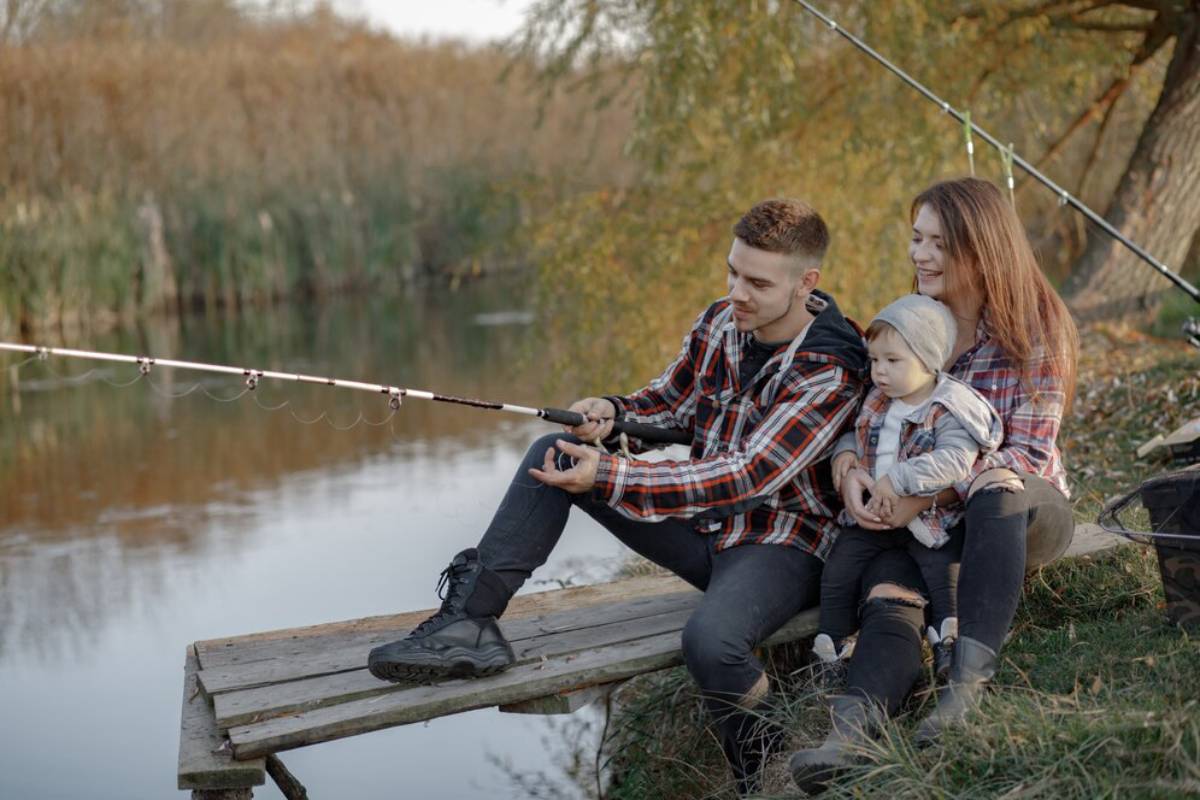 A young family fishing together on a wooden dock by a serene river during autumn.