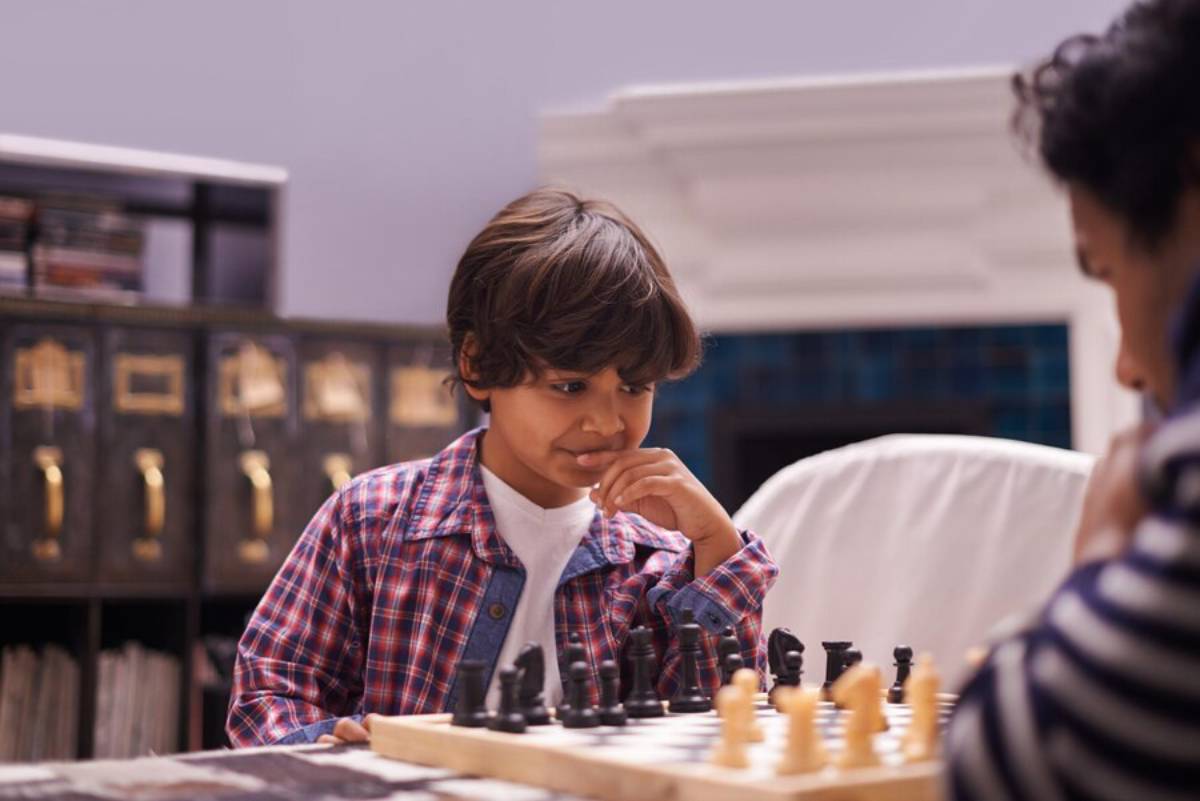 Young boy deeply focused while playing chess with an adult in a cozy living room.