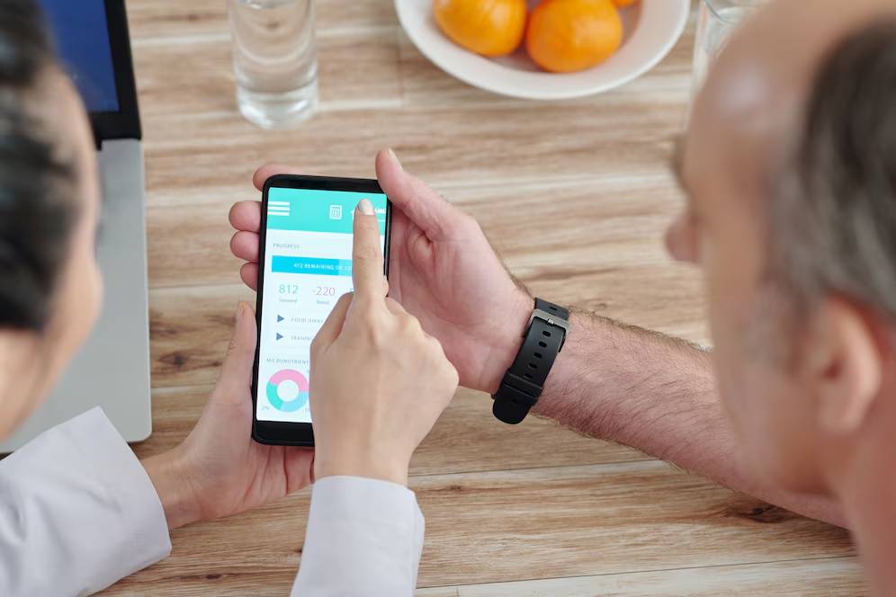 A person discusses app features on a smartphone, while another points at the screen, with citrus fruits in the background.