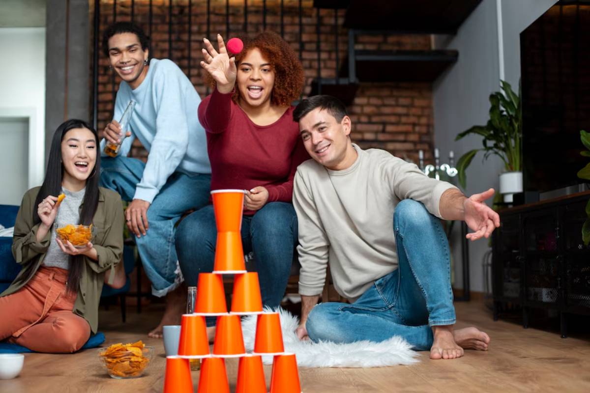 Four friends play a cup stacking game in a cozy living room, laughing and enjoying snacks.