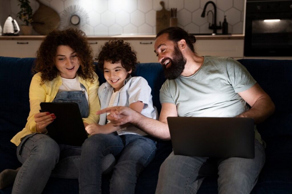 Family enjoys time together using digital tablets and laughing on a living room sofa.