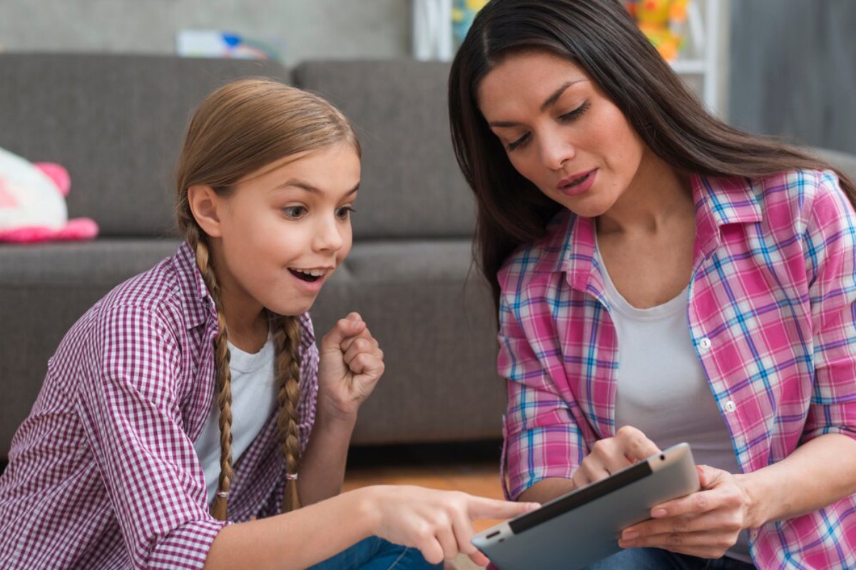 A woman and a girl sit on the floor, focusing intently on a tablet, sharing an engaging moment together in a cozy setting.