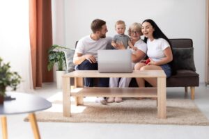 A family with a child gathered on a sofa, engaging with a laptop on a wooden coffee table in a bright, cozy room.