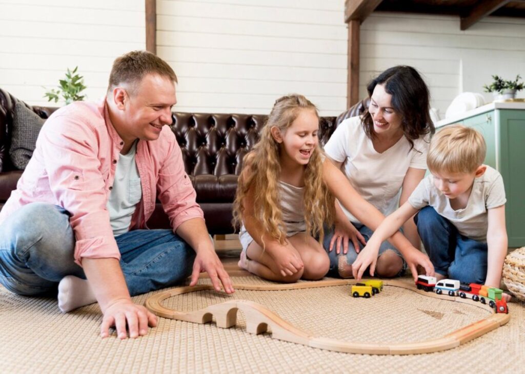 Family playing with a wooden train set on the floor in a cozy living room.