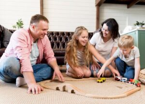 Family playing with a wooden train set on the floor in a cozy living room.