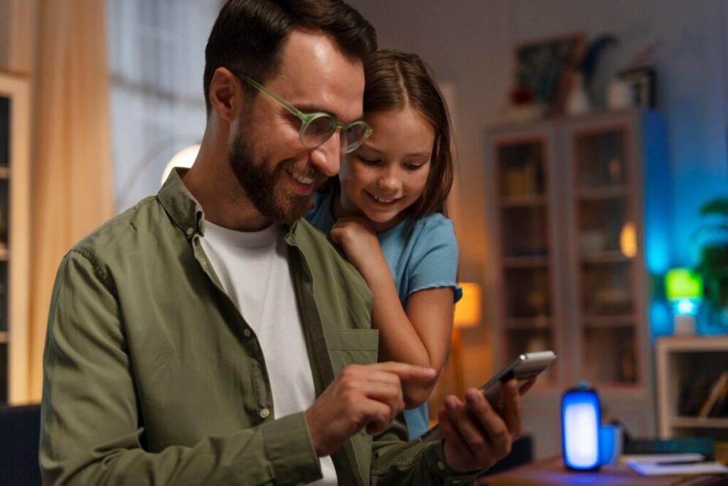 A person in a green shirt interacts with a smartphone while a child leans on them, surrounded by a cozy, softly lit room.